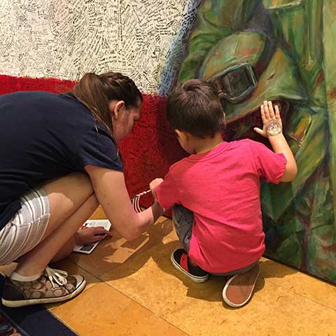 Young woman and her son writing hero message on Hometown Hero installation at ArtPrize Ten